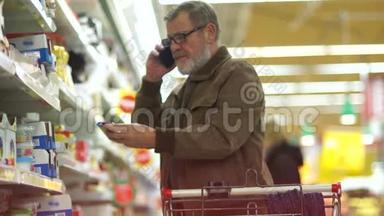 退休人员在超市购物，打电话。 男人在奶酪部门买东西